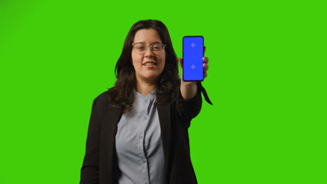 Smiling-Young-Businesswoman-Holding-Blue-Screen-Mobile-Phone-Towards-Camera-Standing-Against-Green-Screen-Background-1